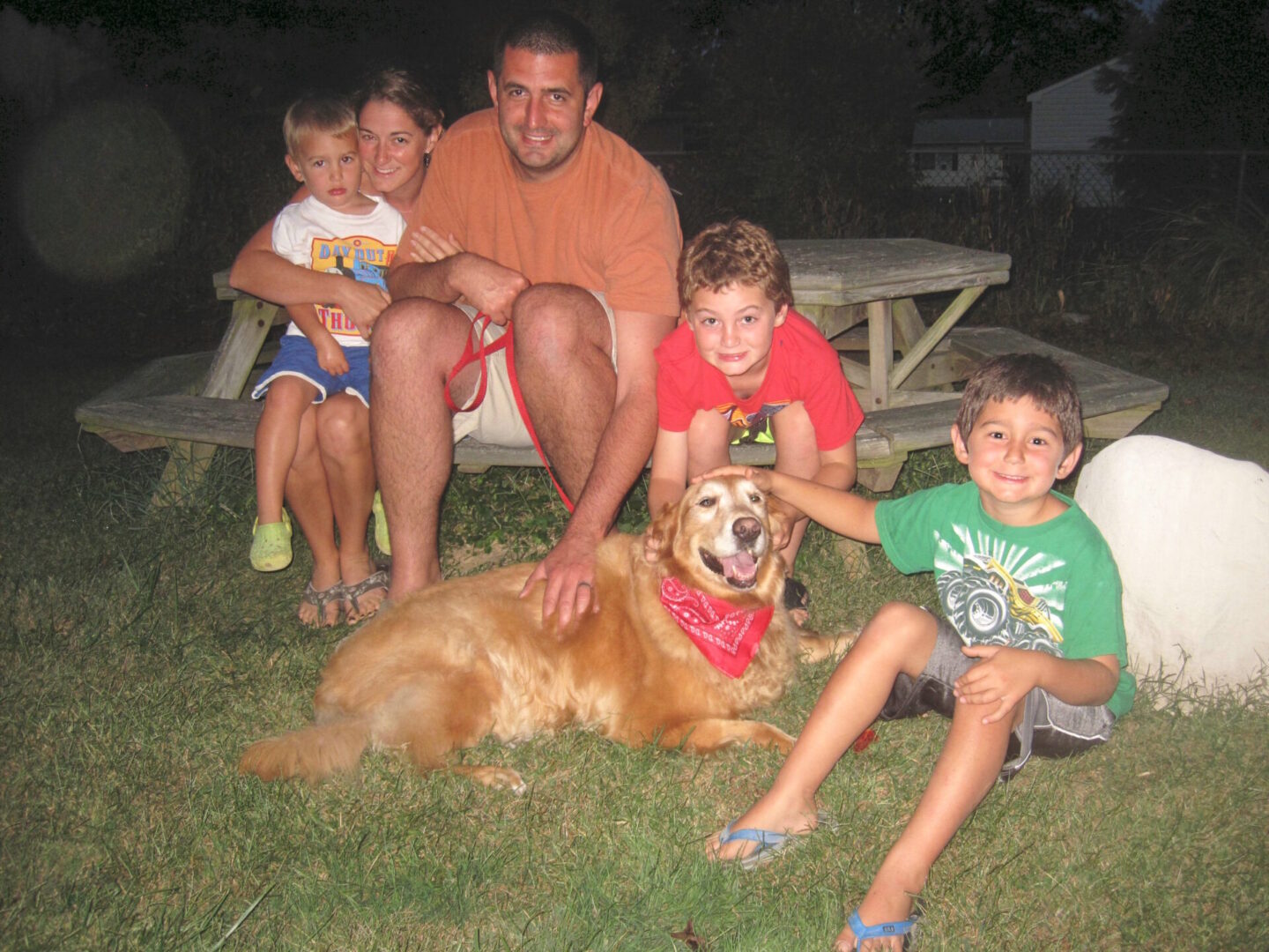 A family with three children and a golden retriever dog posing together outdoors at dusk.