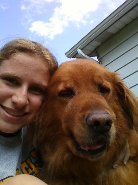 A person posing for a selfie with a happy golden retriever outdoors.