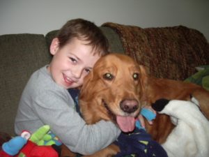 Young boy smiling and cuddling with a golden retriever on a couch.
