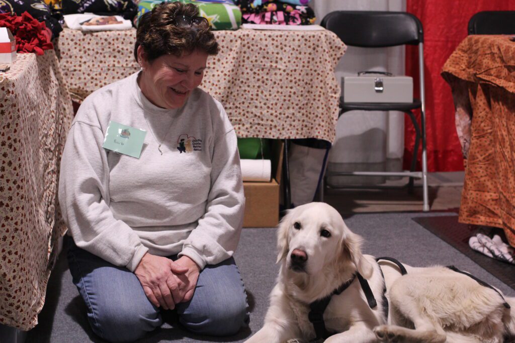 A woman sitting on the floor beside a white dog at an indoor event.