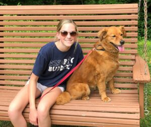 A girl sitting on a wooden bench with a golden retriever.